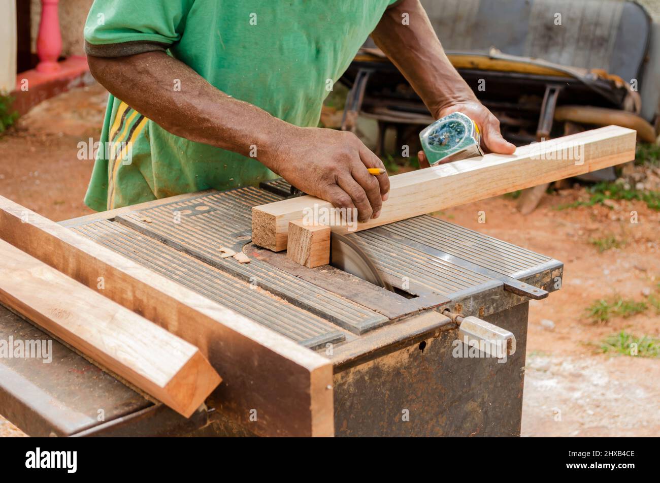 Ein Kabinenmacher mit einem Pencel zwischen den Fingern stützt ein Stück Holz, während er mit einer alten elektrischen Säge sein Ende schneidet Stockfoto