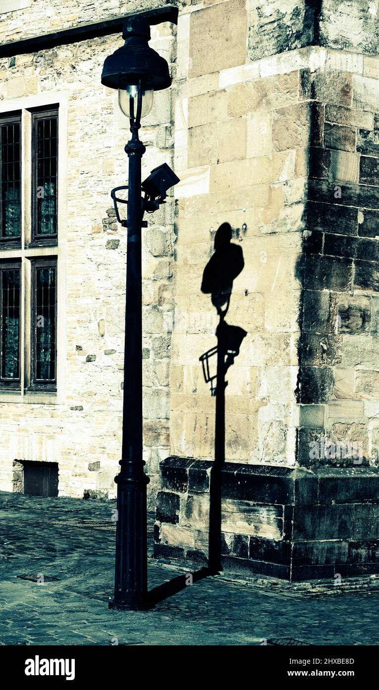 Eine altmodische elektrische Straßenlampe steht vor einer alten schmutzigen Wand und wirft ihren Schatten auf das Sandsteingebäude Stockfoto