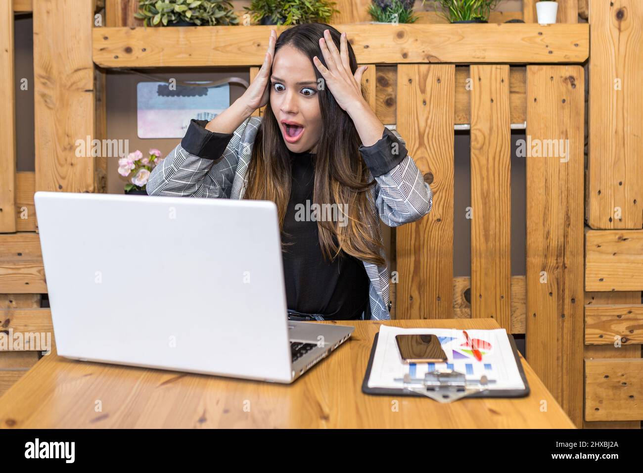 Erstaunte junge Freiberuflerin mit Kopf und Öffnung des Mundes beim Lesen überraschender Daten auf dem Netbook-Bildschirm während der Fernarbeit im Café Stockfoto