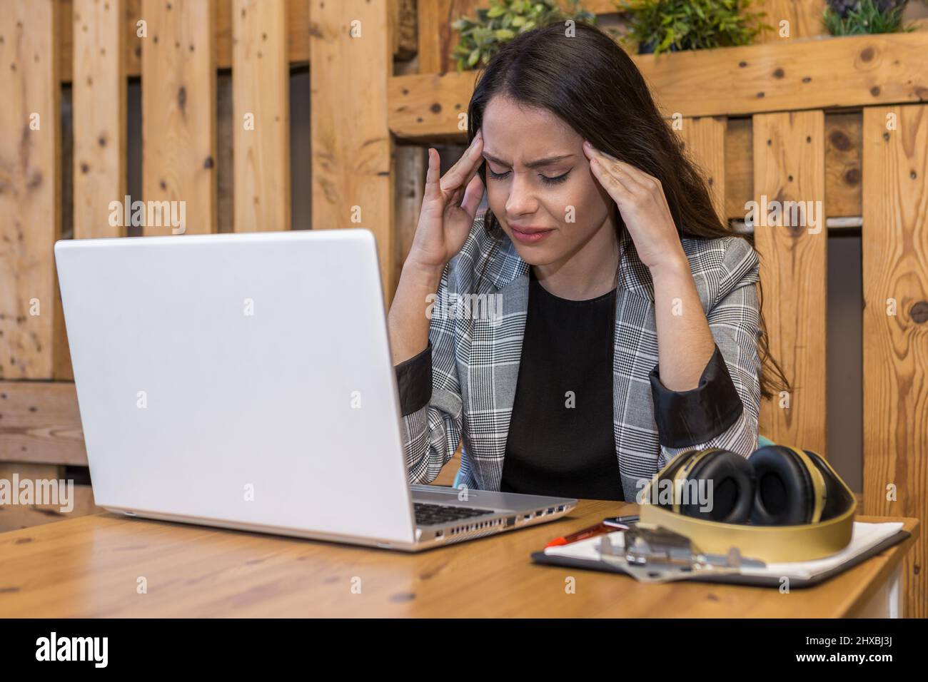 Müde junge Fernarbeiterin, die Kopfschmerzen hatte, während sie im Café an einem Netbook mit Clipboard und kabellosen Kopfhörern arbeitete Stockfoto