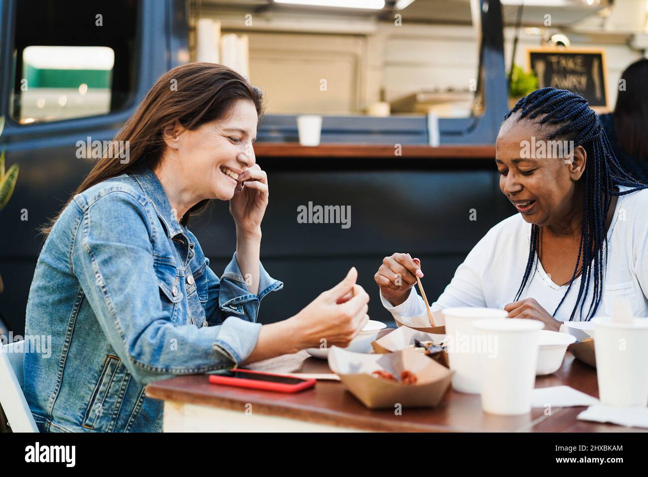 Multirassische Frauen essen im Food Truck Restaurant im Freien - Fokus auf afrikanisches weibliches Ohr Stockfoto