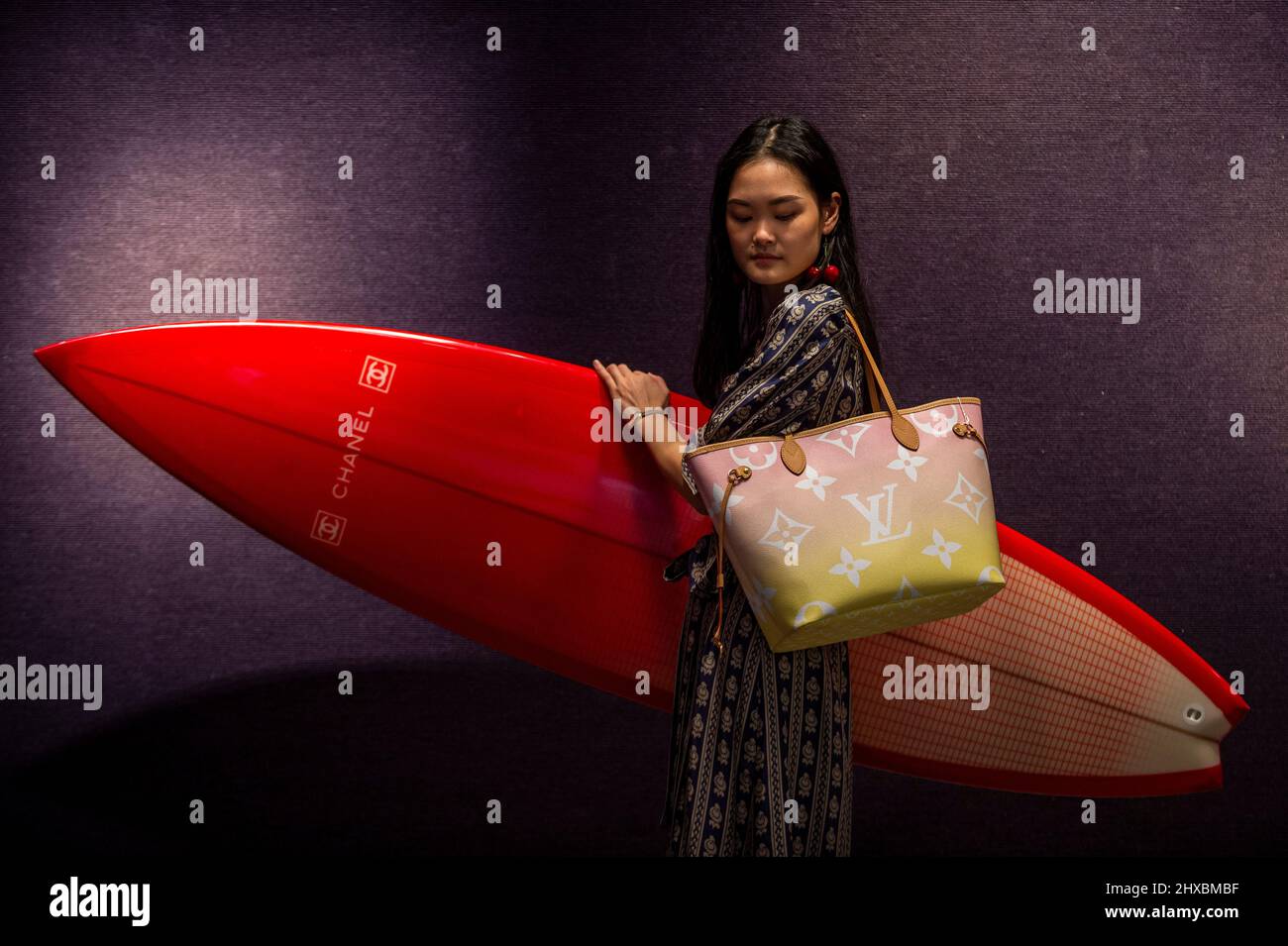 London, UK. 11 March 2022. A staff member presents a red carbon fibre Chanel  Surfboard with three keels (Est. £2,000 – 3,000) and a Louis Vuitton light  pink Monogram Giant 'By the