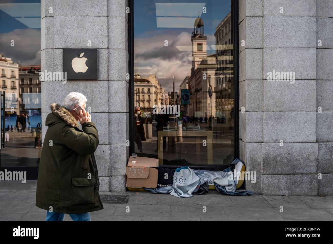 Ein Mann geht an einem Apple-Laden in der Innenstadt von Madrid vorbei, während ein Obdachloser unter Decken schläft Stockfoto