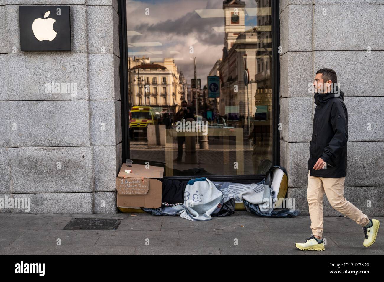 Ein Mann geht an einem Apple-Laden in der Innenstadt von Madrid vorbei, während ein Obdachloser unter Decken schläft Stockfoto