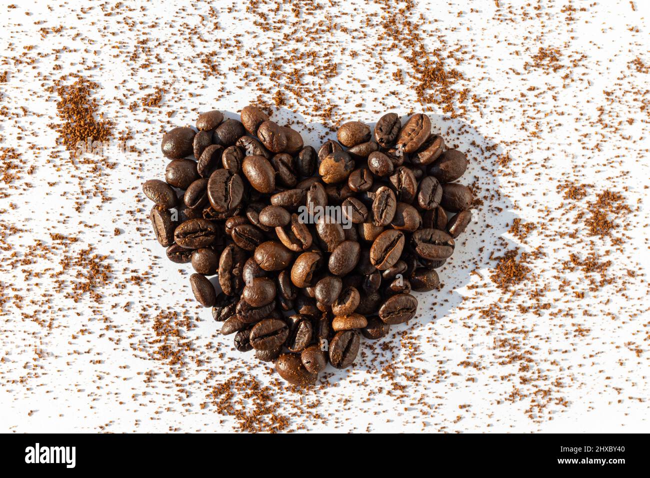 Herzform aus braunen gerösteten Kaffeebohnen Robusta, Arabica-Kaffee auf einem Hintergrund aus gemahlenem Kaffee auf weißem Hintergrund. Kaffee Liebe Konzept Stockfoto