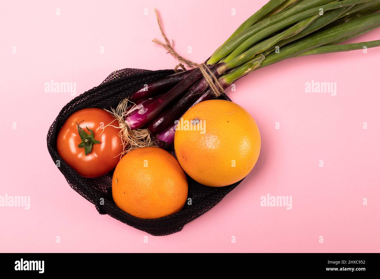 Nahaufnahme von Orangen mit Tomaten und Frühlingszwiebel in schwarzem Netz auf rosa Hintergrund Stockfoto