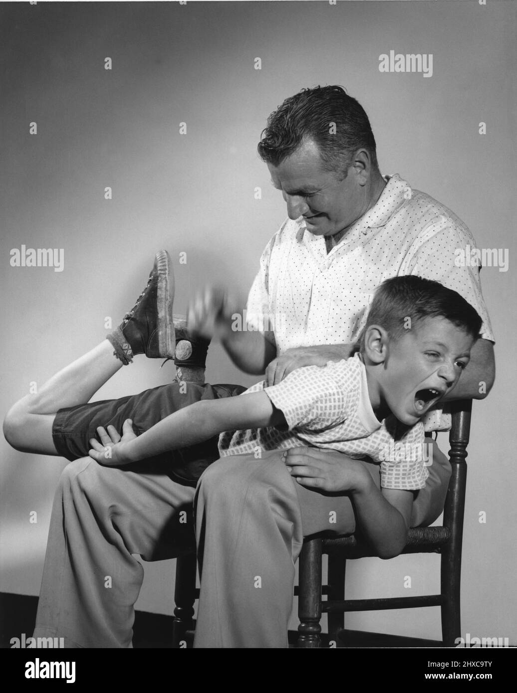 Papa versohlen seinen Sohn, der über seinen Schoß drapiert und brüllend brüllt, während er seine fällig wird Stockfoto