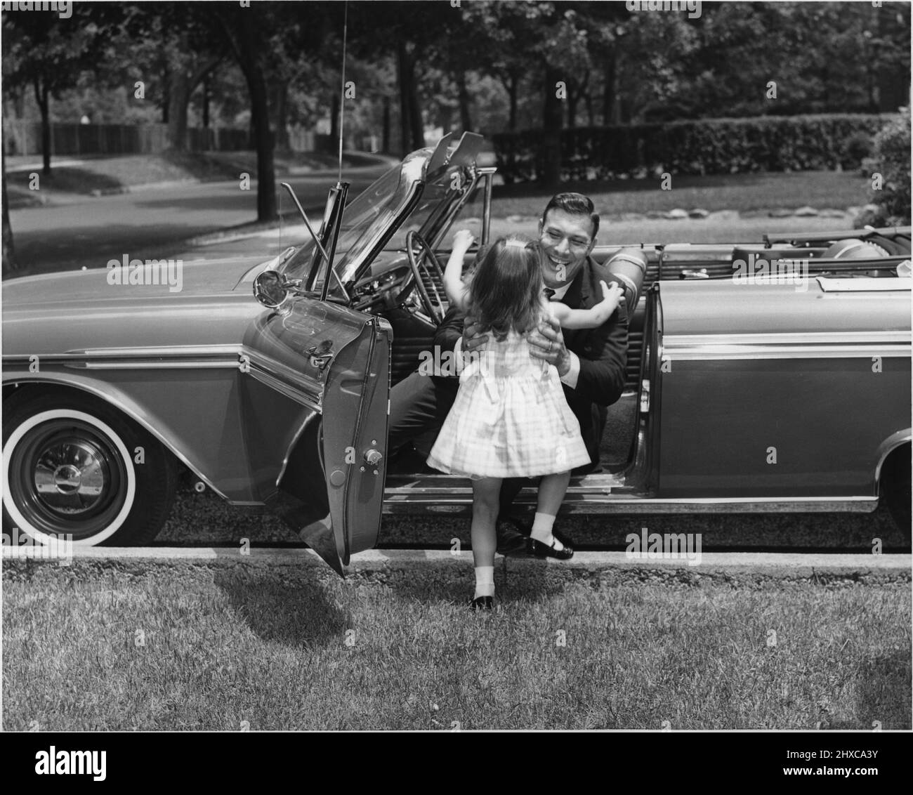 Das kleine Mädchen in einem Kleid rennt, um den Vater zu begrüßen, der gerade in einem Cabriolet fuhr Stockfoto
