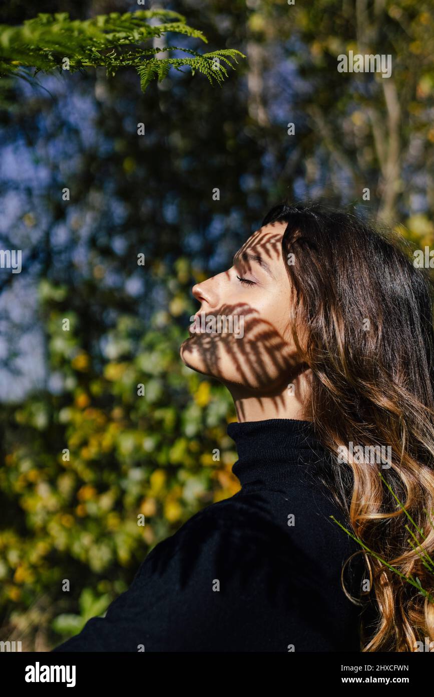 Junge Frau im Profil genießt den sonnigen Tag mit geschlossenen Augen Stockfoto