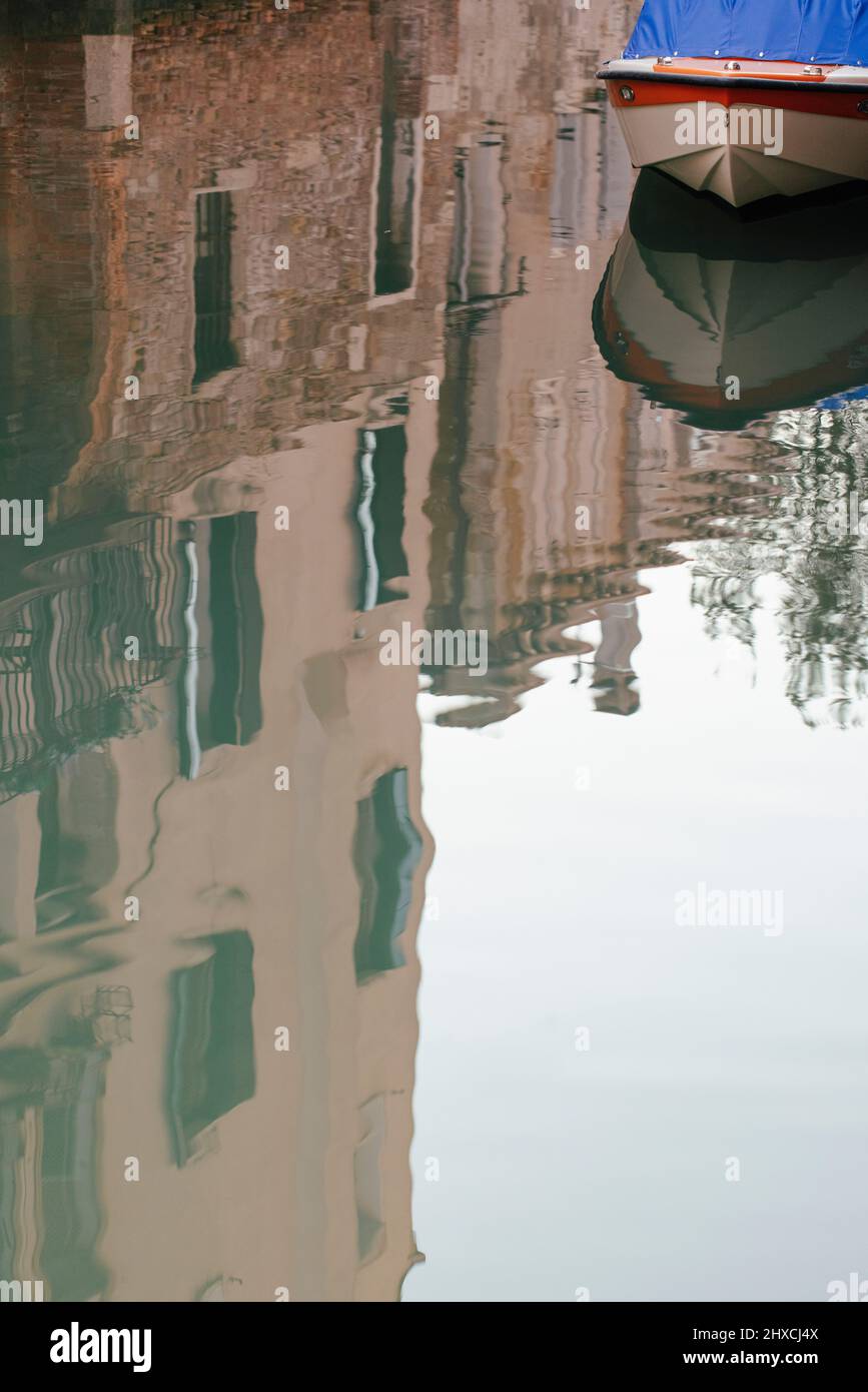 Kleines Motorboot auf einem Kanal in Venedig mit den umliegenden Gebäuden, die sich auf der Wasseroberfläche spiegeln Stockfoto