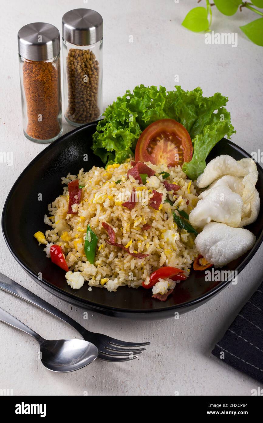 Würzige asiatische gebratene Reis rühren braten mit geräuchertem Rindfleisch, schneiden Sie frische rote Tomaten, frischen grünen Salat und weiße Cracker in schwarzen ovalen Teller Stockfoto