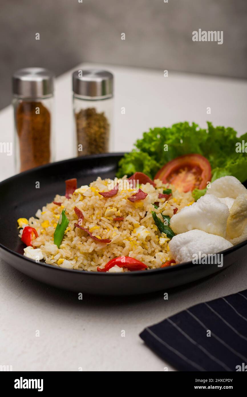 Würzige asiatische gebratene Reis rühren braten mit geräuchertem Rindfleisch, schneiden Sie frische rote Tomaten, frischen grünen Salat und weiße Cracker in schwarzen ovalen Teller Stockfoto