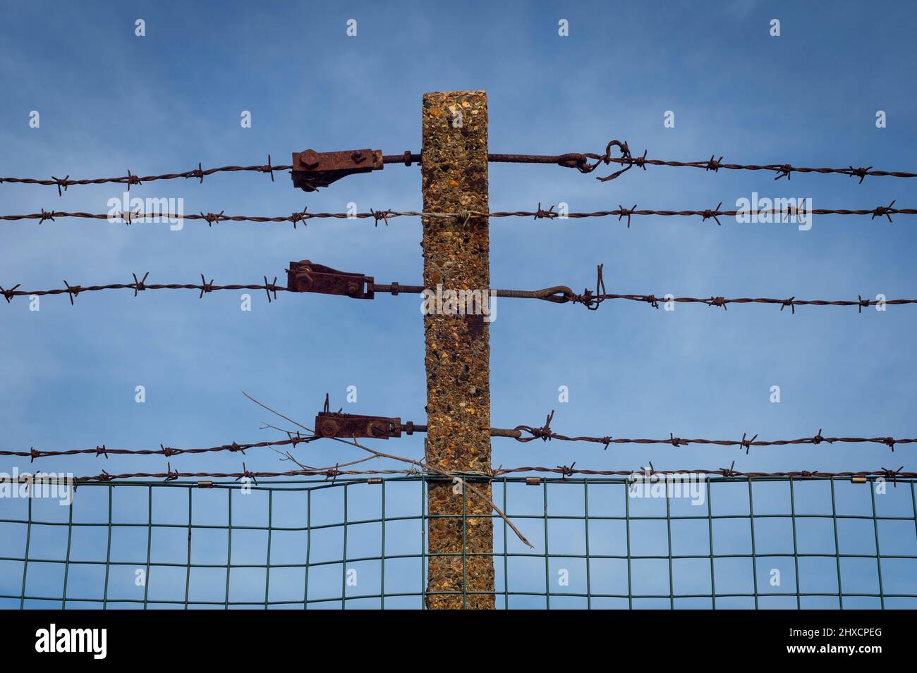 Rostiger Stacheldrahtzaun mit blauem Himmel Hintergrund Stockfoto