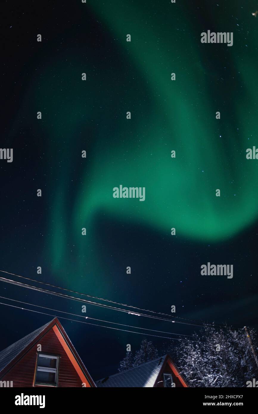 Polarlichter tanzen über roten Holzkabinen in Norwegen Stockfoto