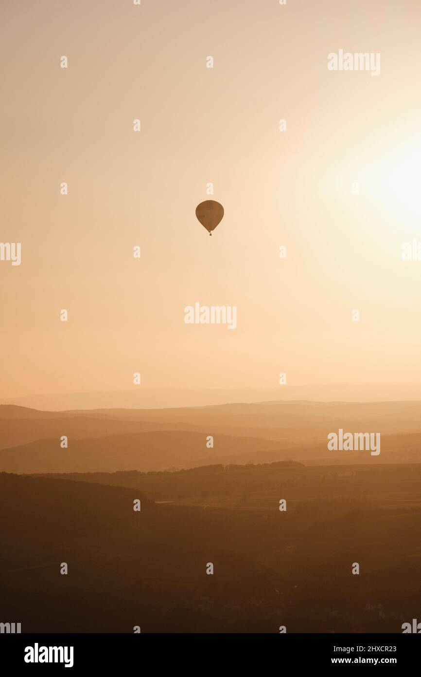 Ballon, der während des Sonnenuntergangs über dem Tal mit Hügelschichten fliegt Stockfoto