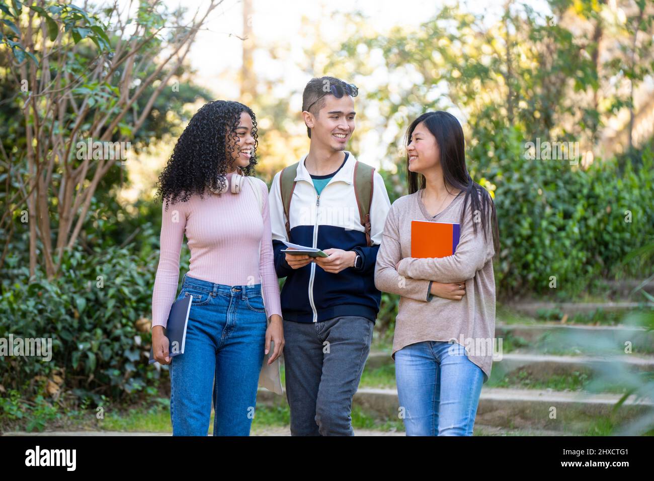 Drei junge multiethnische Studenten, die auf der Straße spazieren und sich unterhalten Stockfoto