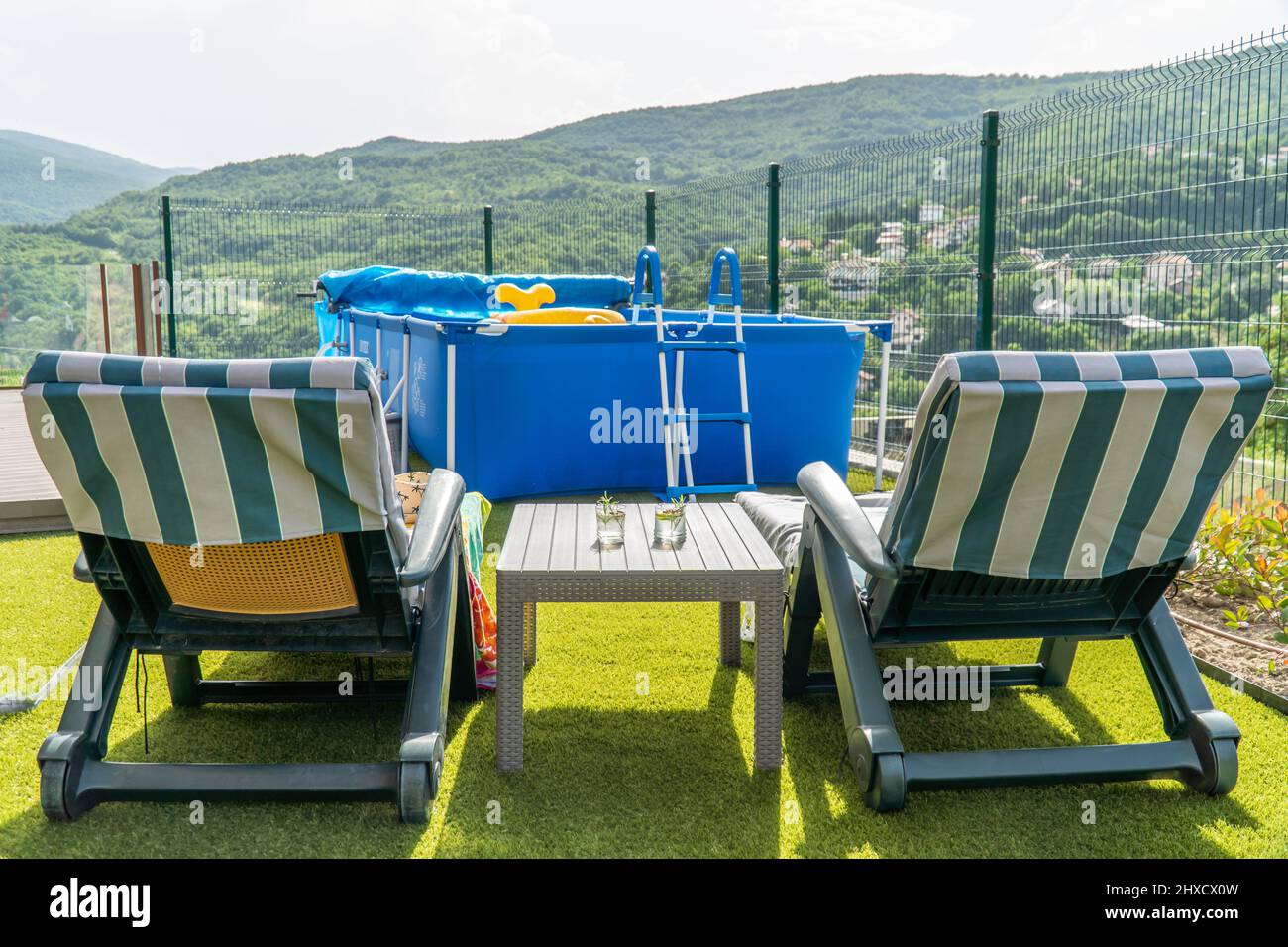 Zwei Sonnenliegen mit Cocktails auf einem Tisch und ein Swimmingpool im Hintergrund Stockfoto