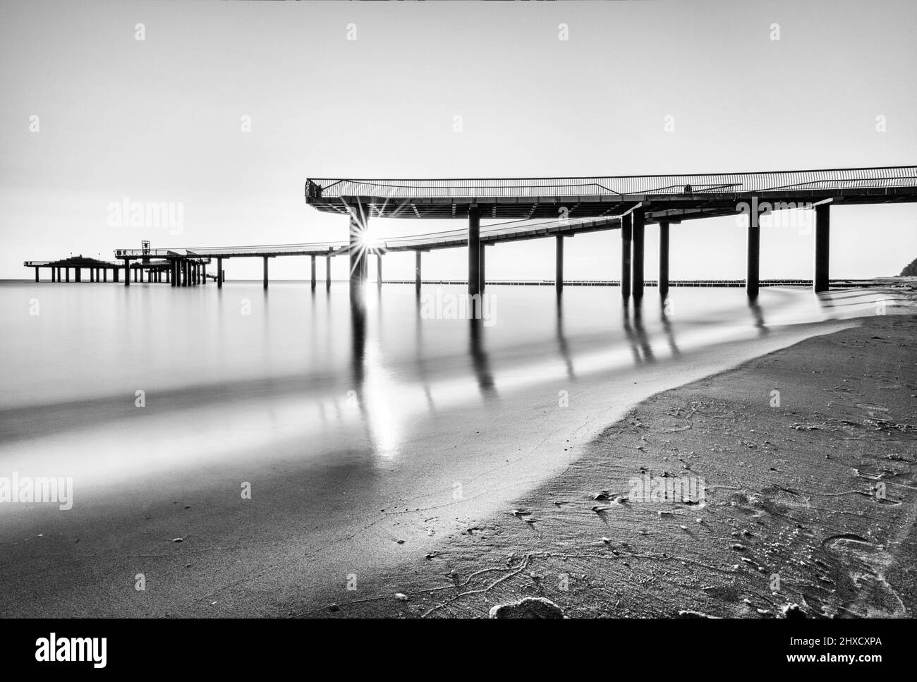 Der neue Pier in Koserow mit seiner Wellenform bei Sonnenaufgang in Langzeitbelichtung und Schwarz-Weiß Stockfoto