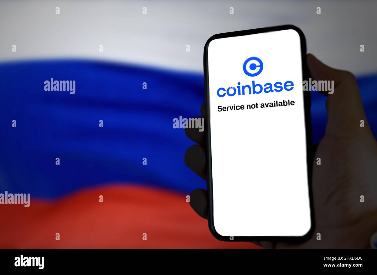 Moskau, RUS, 2022. März: Hand hält ein Telefon, während die Coinbase-App außer Betrieb ist und die russische Flagge im Hintergrund verschwommen ist. Im März Stockfoto