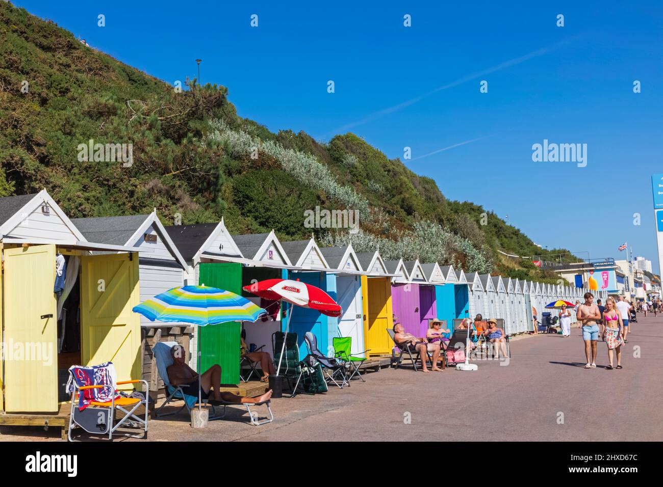 England, Dorset, Bournemouth, Bournemouth Beach, Menschen, die vor einer Reihe von farbenfrohen Strandhütten sonnenbaden Stockfoto