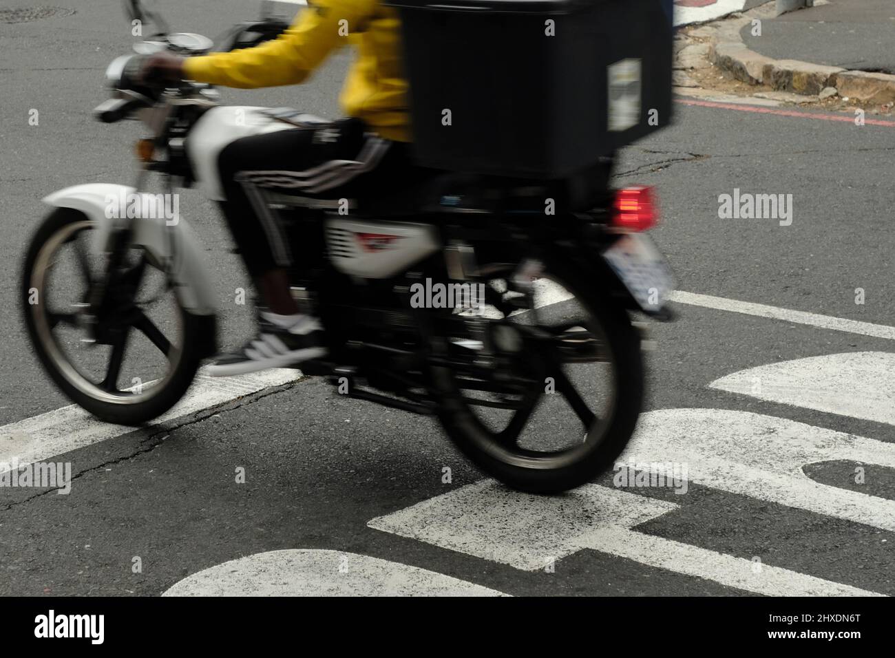 Das Liefermotorrad beschleunigt von einer Stoppstraße weg, um ein Paket zuzustellen. Stockfoto