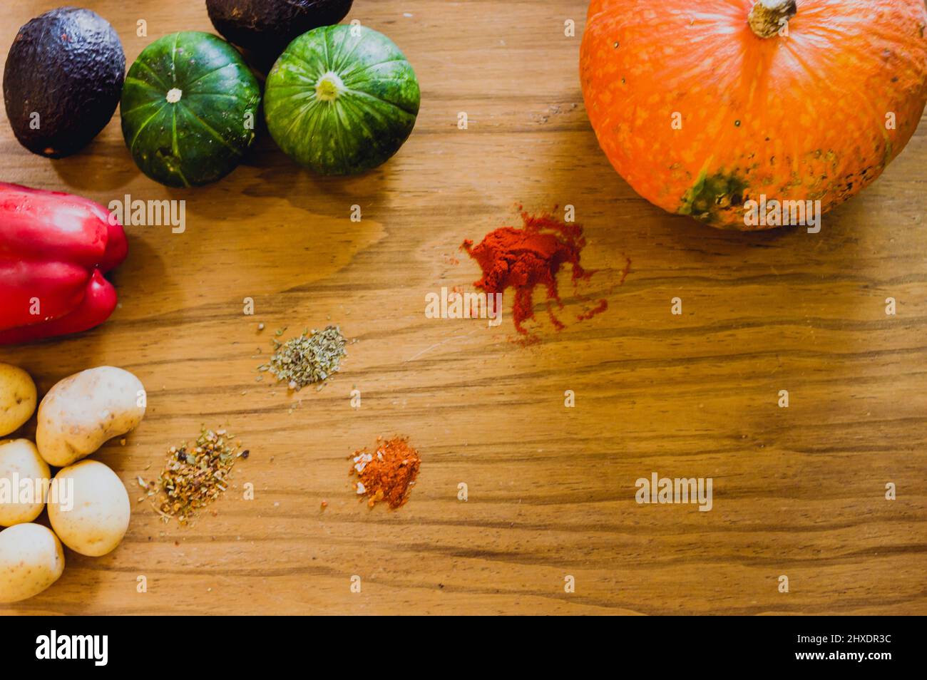 Draufsicht auf Kürbis, Zucchini, Kartoffeln, Paprika, Avocado, Kreuzkümmel, Olegano, Thymian, pflanzliche Zutaten und Gewürze, um eine Suppe auf einem Holzboden zu machen Stockfoto