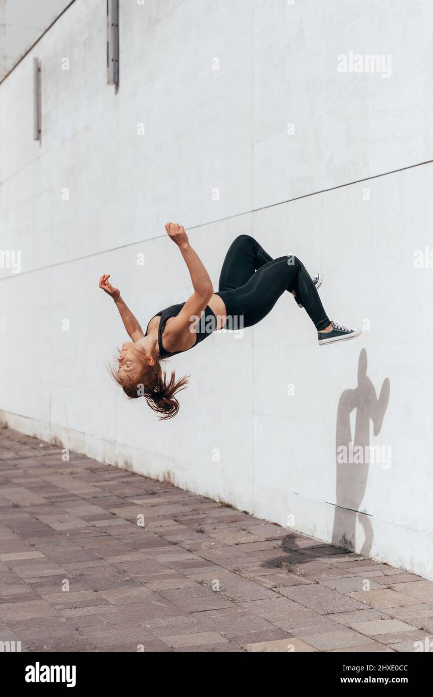 Mädchen, die auf dem städtischen Platz einen Parkour-Backflip machen. Sport Lifestyle Frauen tun acrobat Trick in der Stadt. Vertikales Foto Stockfoto