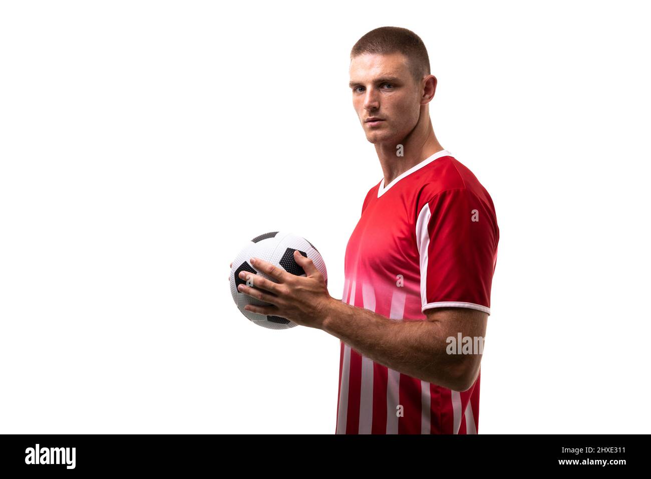 Seitenansicht Porträt eines selbstbewussten männlichen kaukasischen Fußballspielers, der den Ball auf weißem Hintergrund hält Stockfoto