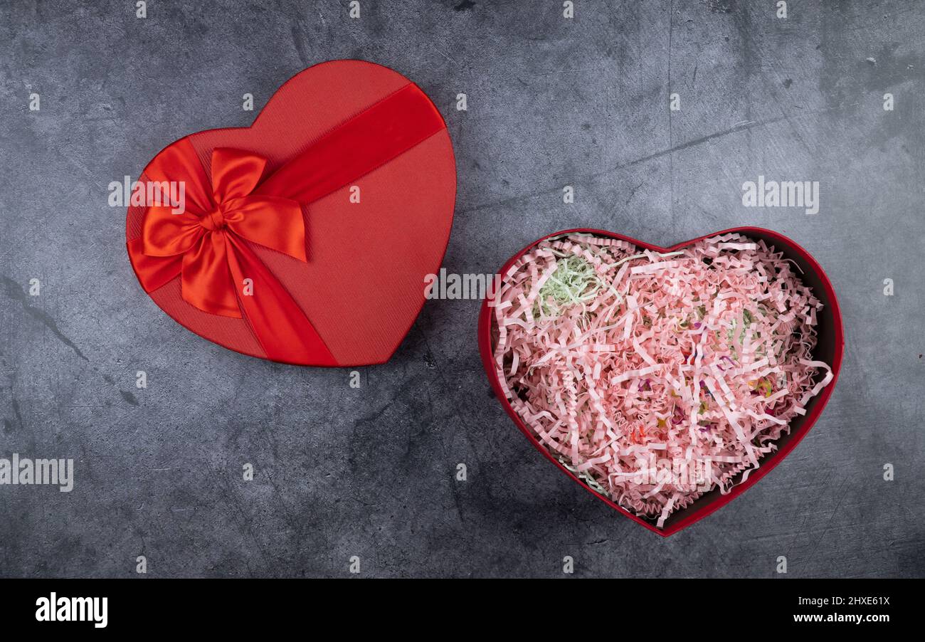 Rote Schachtel in Herzform auf dunklem Hintergrund. Festliche Verpackung für romantische Geschenke. Obere Ansicht, Kopierraum. Stockfoto