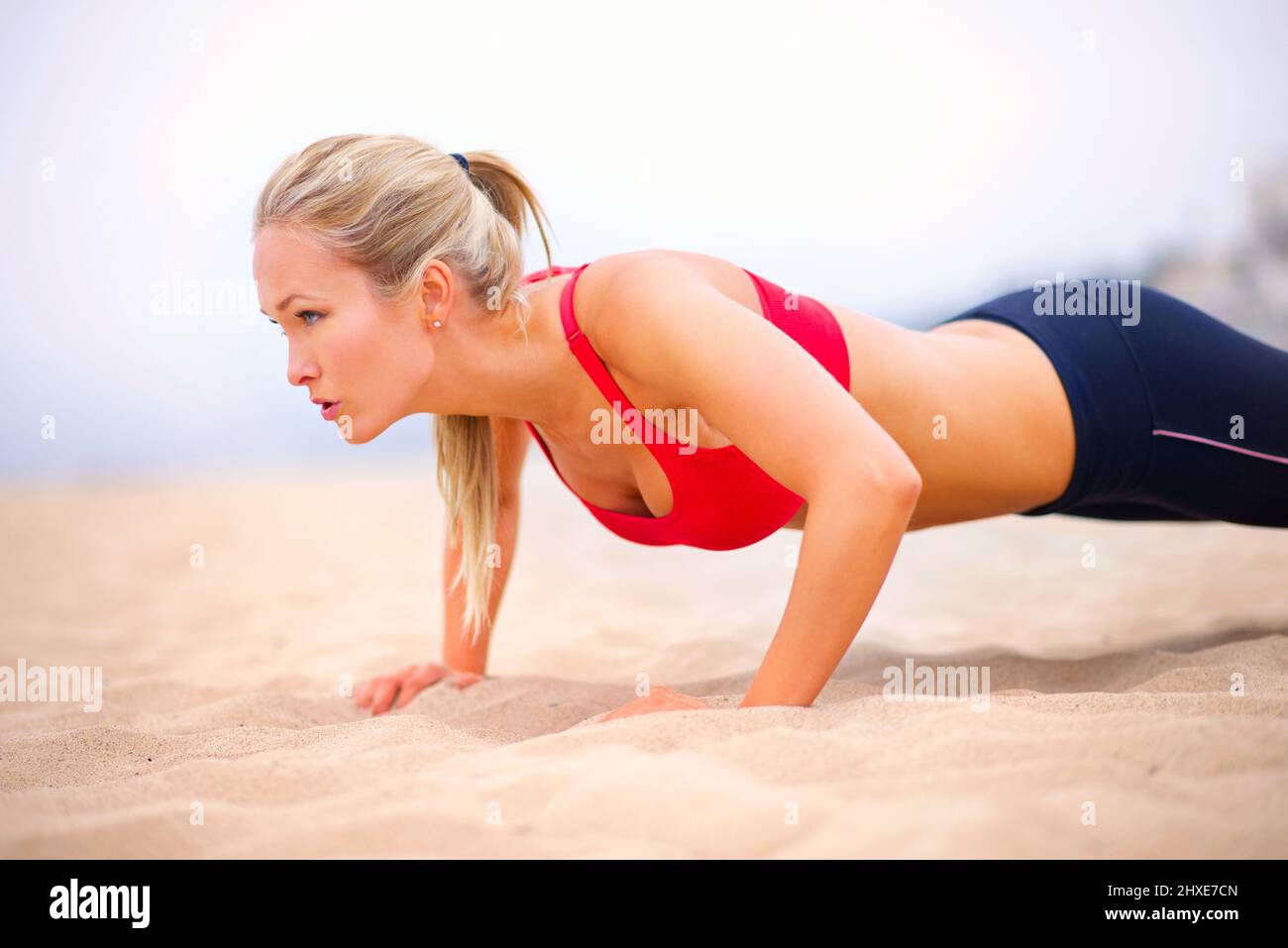 Ganzkörpergesundheit. Aufnahme einer jungen Frau in Sportkleidung, die Liegestütze am Strand macht. Stockfoto