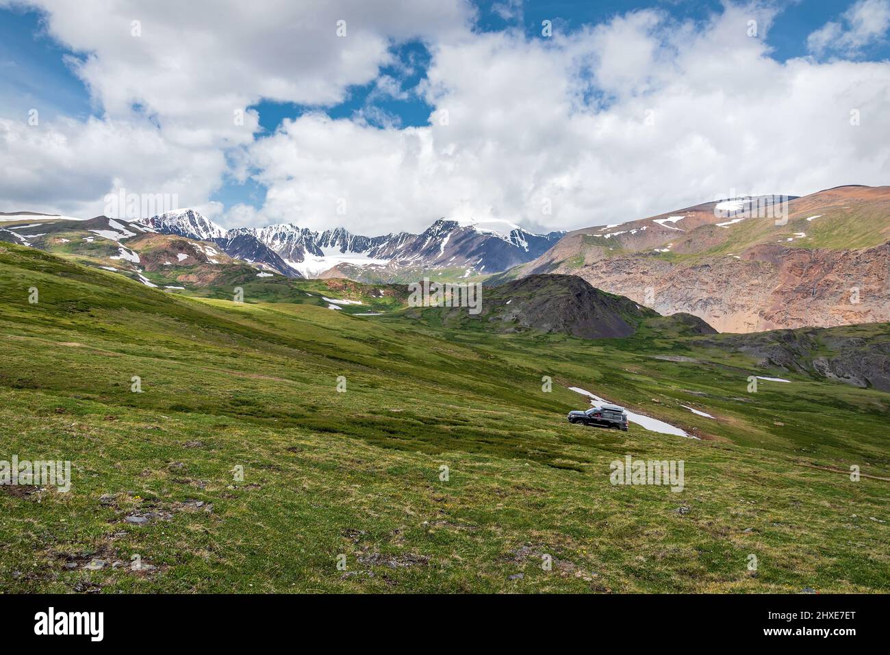 Herrliche Aussicht auf den Sommer mit schneebedeckten Bergen, Gletscher, grünem Gras, Feldweg und Auto gegen blauen Himmel und Wolken. Altai, Russland Stockfoto