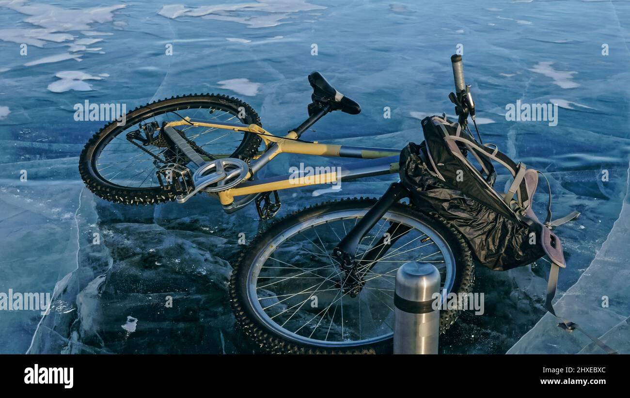 Mann und Fahrrad auf Eis. Er schaut auf das schöne Eis in den Rissen. Blick auf die erste Person auf dem Fahrrad. In der Nähe befindet sich eine Thermoskanne und ein Fahrradrucksack. Eis des Th Stockfoto