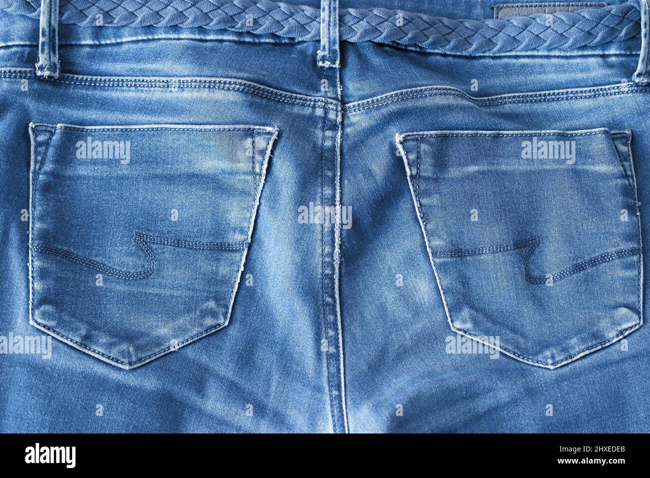 Der obere Teil alter, abgenutzter blauer Jeans mit Taschen und geflochtenem Gürtel Stockfoto