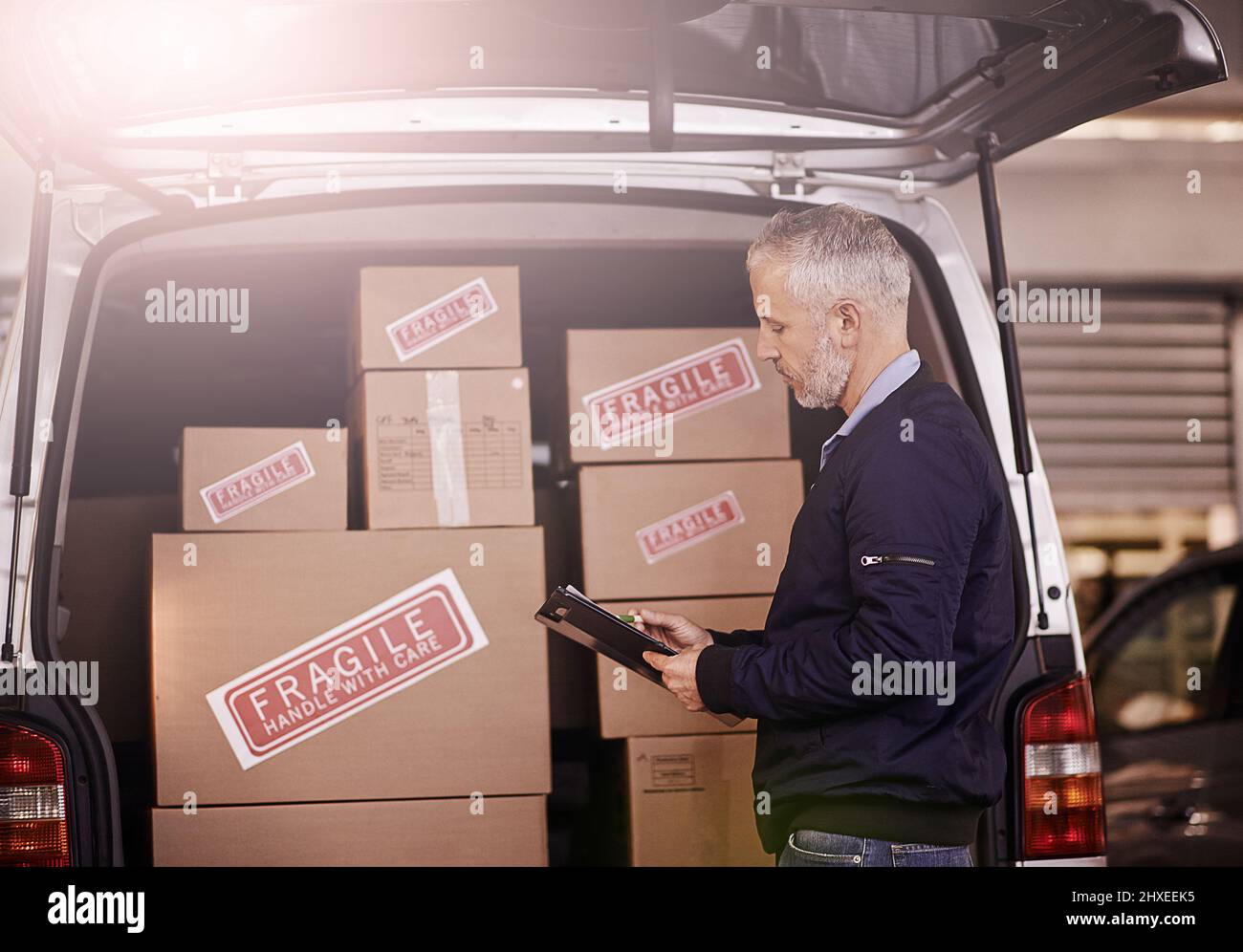 Hier ist alles in Ordnung. Aufnahme eines reifen Lieferers, der neben einem mit Kartons verpackten Lieferwagen stand. Stockfoto