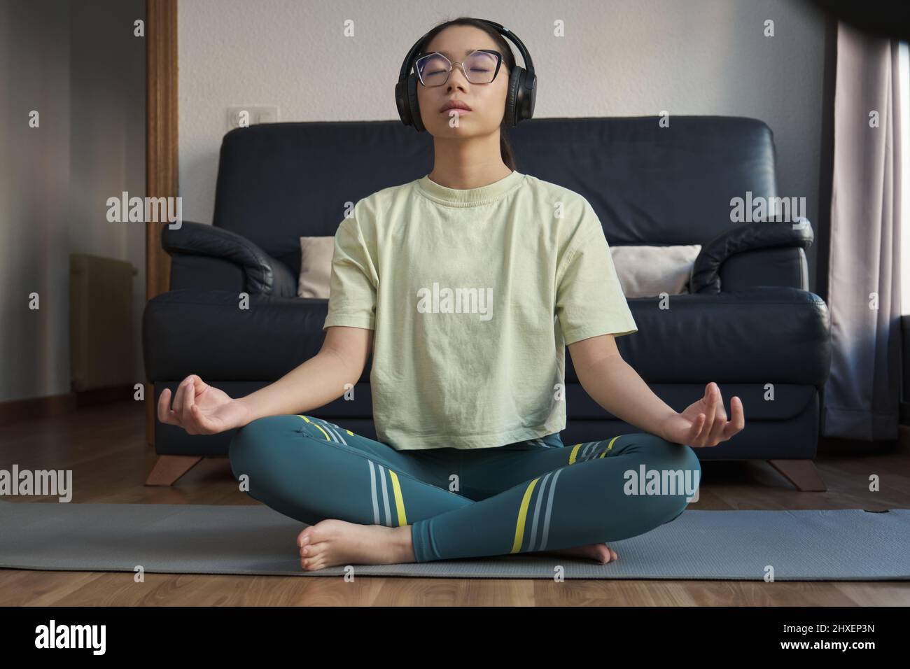 Junge asiatische Frau hört entspannende Musik und meditiert dabei die einfache Pose. Stockfoto