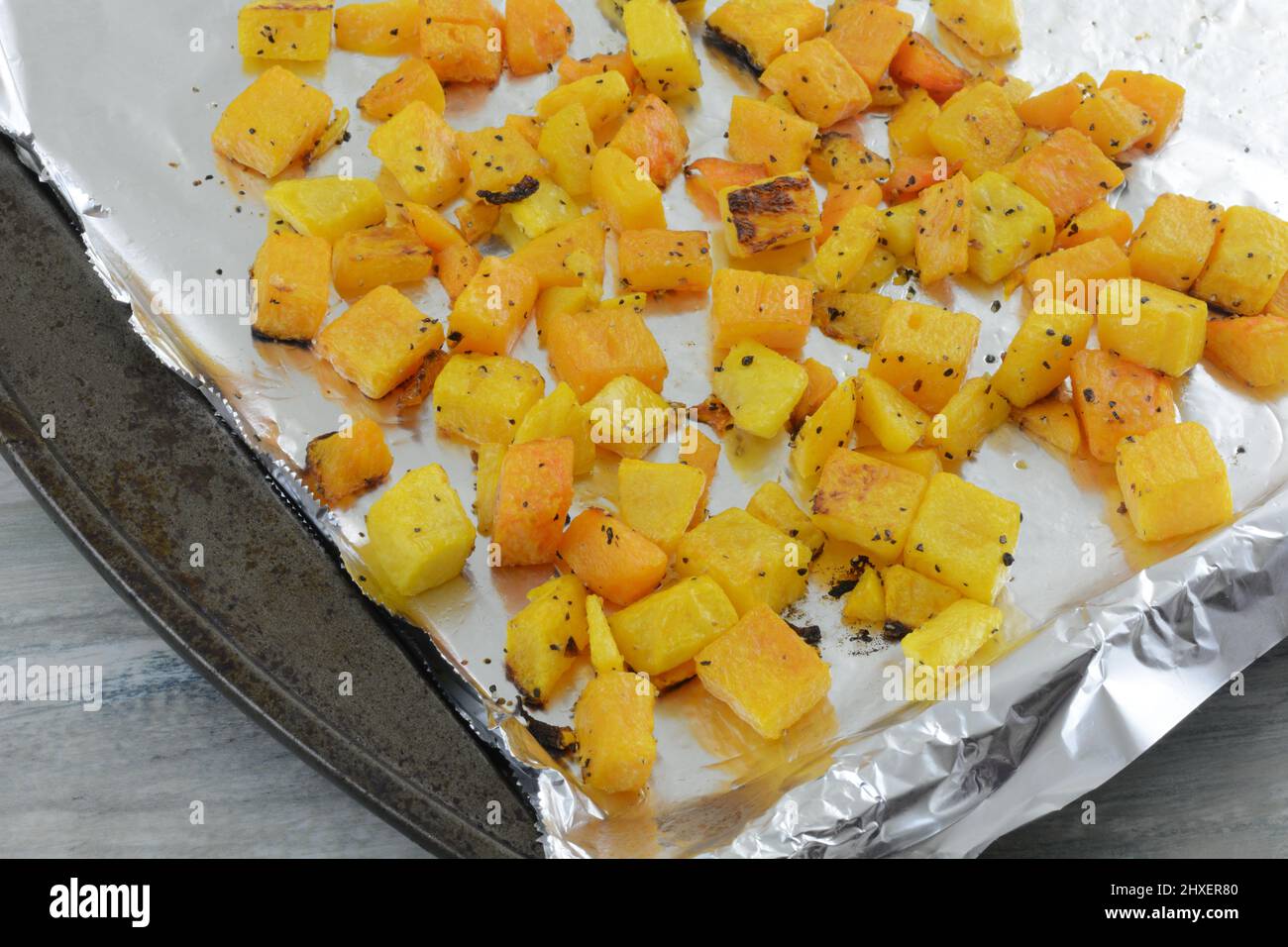 Geröstete Butternut-Squashwürfel mit Gewürzen auf aluminiumfoliengesäumtem Backblech Stockfoto
