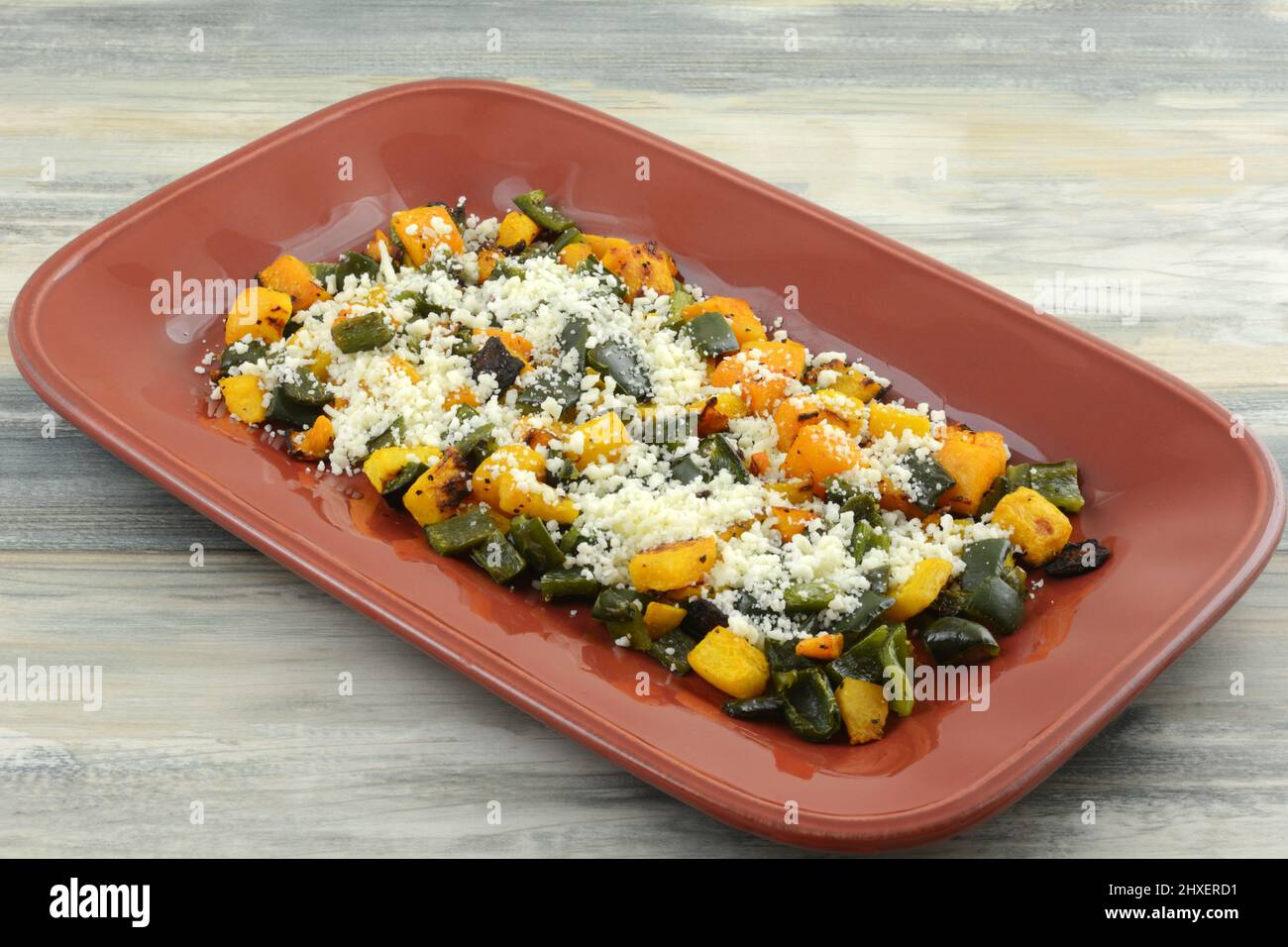 Beilage Butternut-Kürbis und Poblano-Pfeffer auf rotem Servierteller Stockfoto