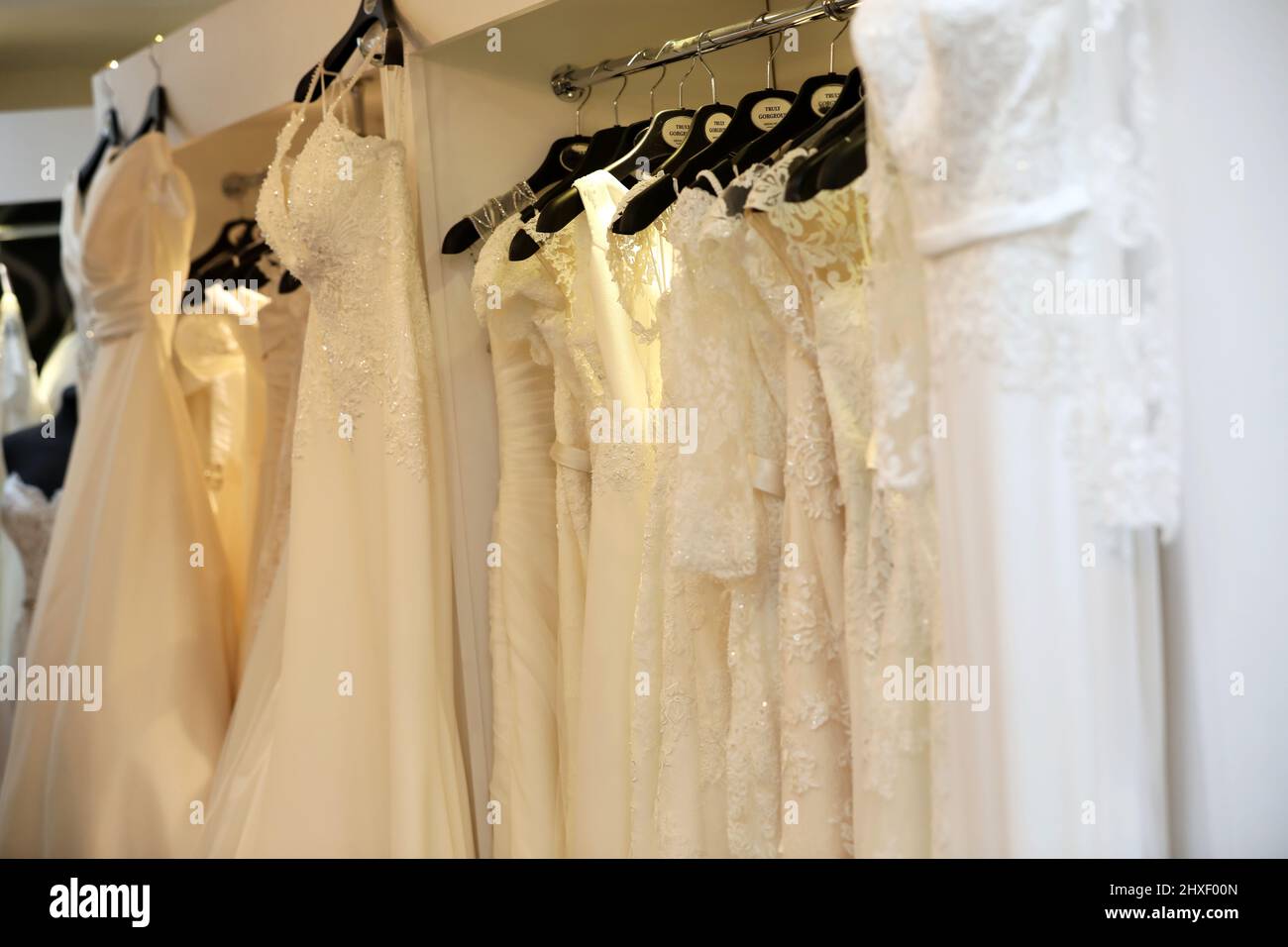Eine Auswahl weißer Hochzeitskleider, die in einem Modegeschäft in Chichester, West Sussex, Großbritannien, abgebildet sind. Stockfoto