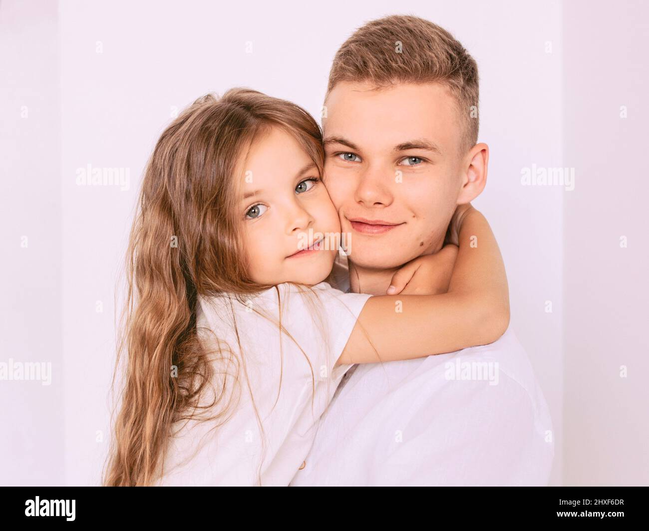 kaukasisch glücklich liebenswert Geschwister - Teenager Junge Bruder und kleines Mädchen Schwester kuscheln auf weißem Hintergrund innen. Familie, Beziehungen, Verwandte, Stockfoto
