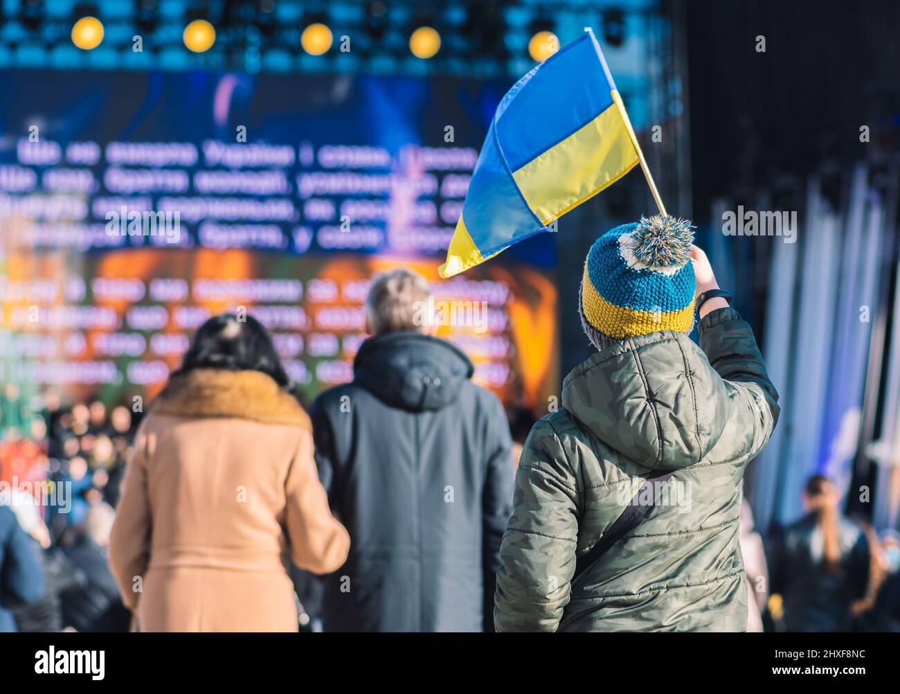 Kind oder Kind mit Winterkleidung und Hut mit ukrainischen Farben. Protest gegen den Krieg in der Ukraine, ausgelöst durch Putin und Russland Stockfoto