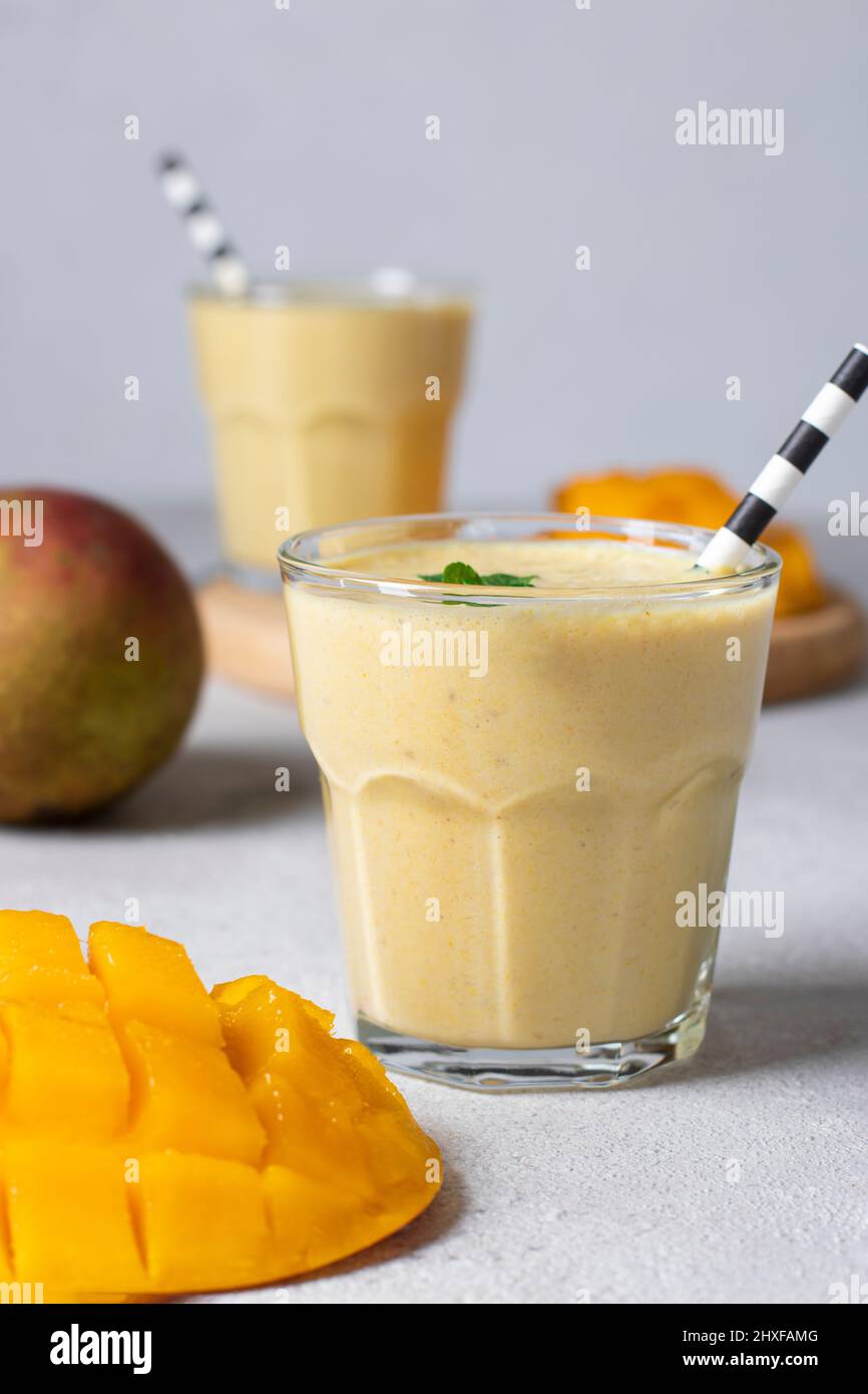 Mango Lassi in zwei Gläsern auf hellgrauem Hintergrund. Frische indischer Lassi aus Joghurt, Wasser, Gewürzen, Mango und Eis Stockfoto