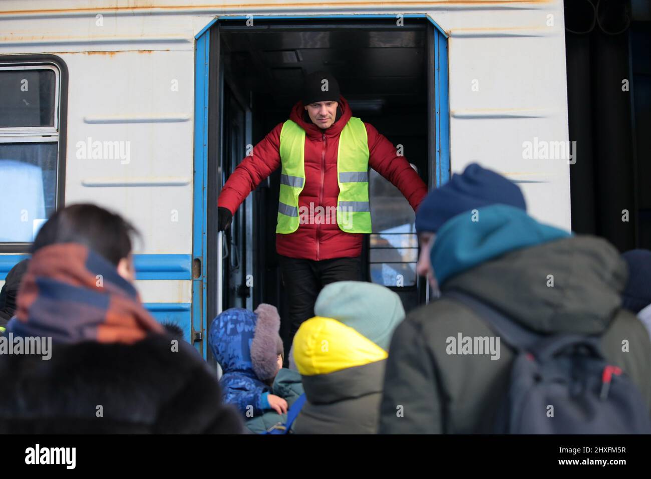 LVIV, UKRAINE - 11. MÄRZ 2022 - Ein Mann in einer High-viz-Jacke steht oben auf der Treppe eines Kutschenmädchen als Menschen, die vor der russischen Invasion fliehen Stockfoto