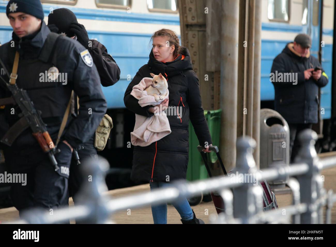 LVIV, UKRAINE - 11. MÄRZ 2022 - Ein Mädchen, das einen Koffer zieht, trägt einen Hund, der in eine Decke gehüllt ist, während Menschen, die vor der russischen Invasion fliehen, auf eine Evakuierung warten Stockfoto