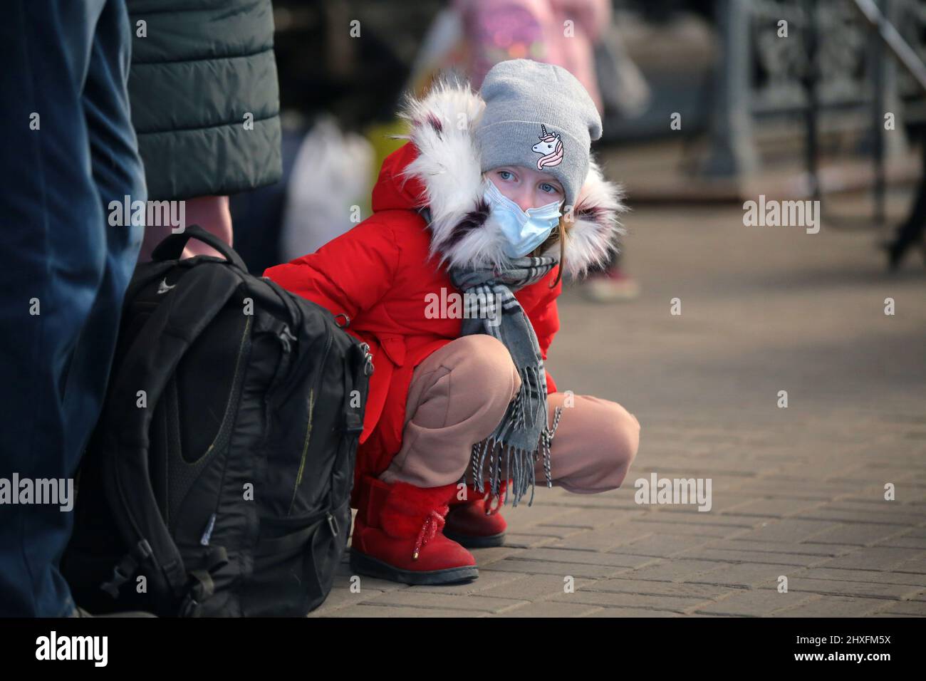 LVIV, UKRAINE - 11. MÄRZ 2022 - Ein Mädchen in einer Gesichtsmaske sitzt auf ihren Geigen an einem Rucksack auf der Plattform, während Menschen vor der russischen Invasion warten Stockfoto