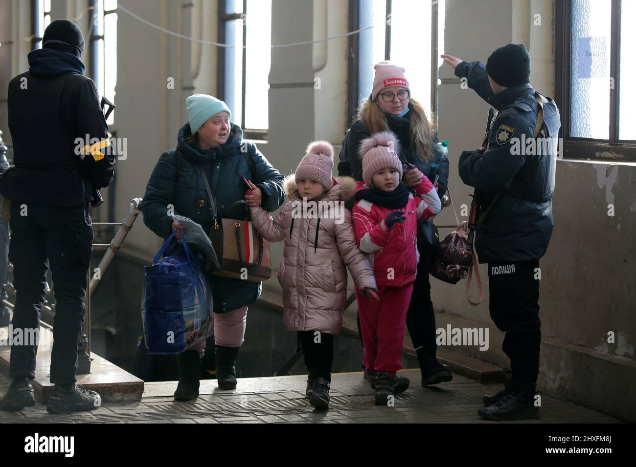 LVIV, UKRAINE - 11. MÄRZ 2022 - Ein Polizeibeamter spricht mit Frauen, die mit Mädchen gehen, während Menschen, die vor der russischen Invasion fliehen, auf einen Evakuierungszug warten Stockfoto