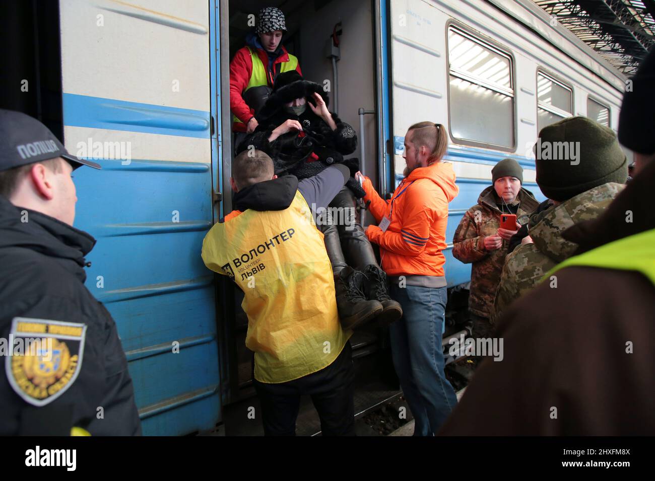 LVIV, UKRAINE - 11. MÄRZ 2022 - drei Männer heben eine Frau mit Behinderungen in einen Zug, während Menschen, die vor der russischen Invasion fliehen, auf einen Evakuierungszug warten Stockfoto