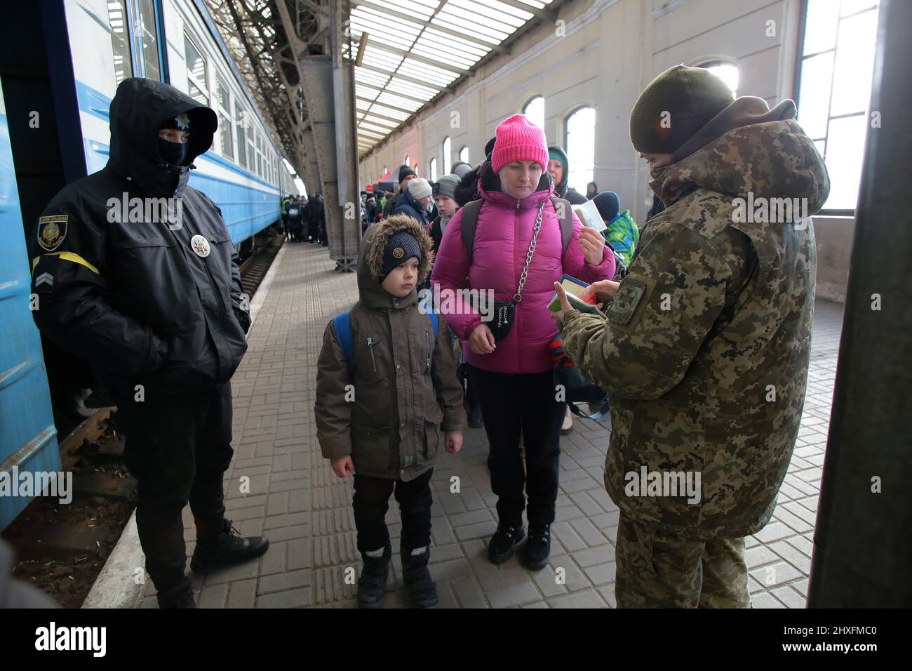 LVIV, UKRAINE - 11. MÄRZ 2022 - Ein Grenzschutz überprüft die Dokumente einer Frau, die mit einem Jungen reist, während Menschen, die vor der russischen Invasion fliehen, auf ein e warten Stockfoto