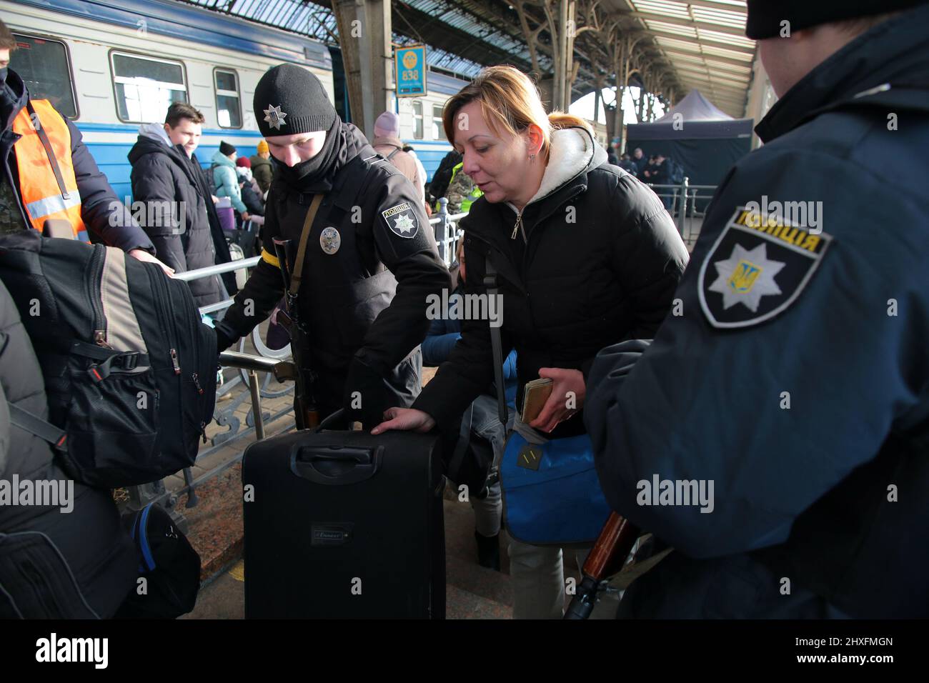 LVIV, UKRAINE - 11. MÄRZ 2022 -Ein Polizeibeamter hilft einer Frau mit ihrem Koffer, während Menschen, die vor der russischen Invasion fliehen, auf einen Evakuierungszug nach P warten Stockfoto