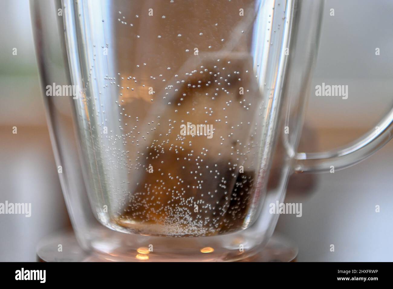 Teebeutel in Wasser brauen - Koffein-Getränk in doppelverglasten Teetassen - Nahaufnahme eines teilweise gebrühten Teebeutels in einer Teetasse mit heißem Wasser Stockfoto