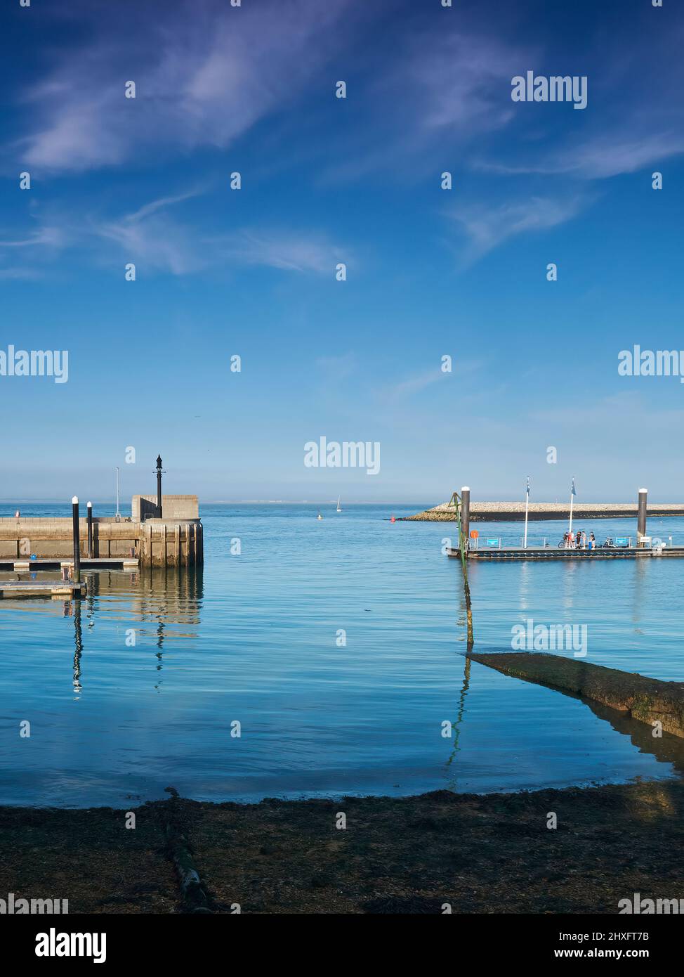 Dennoch, klare, glasige Gewässer in einem Hafen auf der Isle of Wight, bereit, eine ferne Yacht zu empfangen, die ihren Weg unter einem tiefblauen Himmel macht. Stockfoto